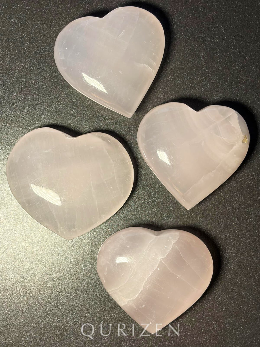Four heart-shaped stones on a reflective surface with 'QURIZEN' branding.