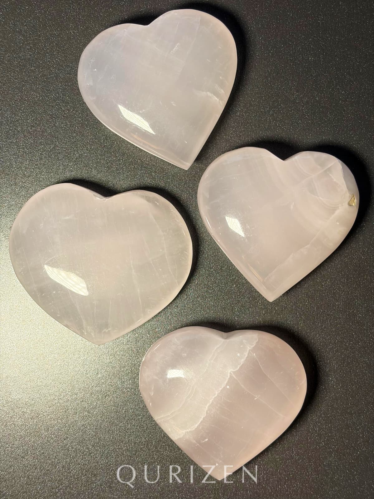 Four heart-shaped stones on a reflective surface with 'QURIZEN' branding.