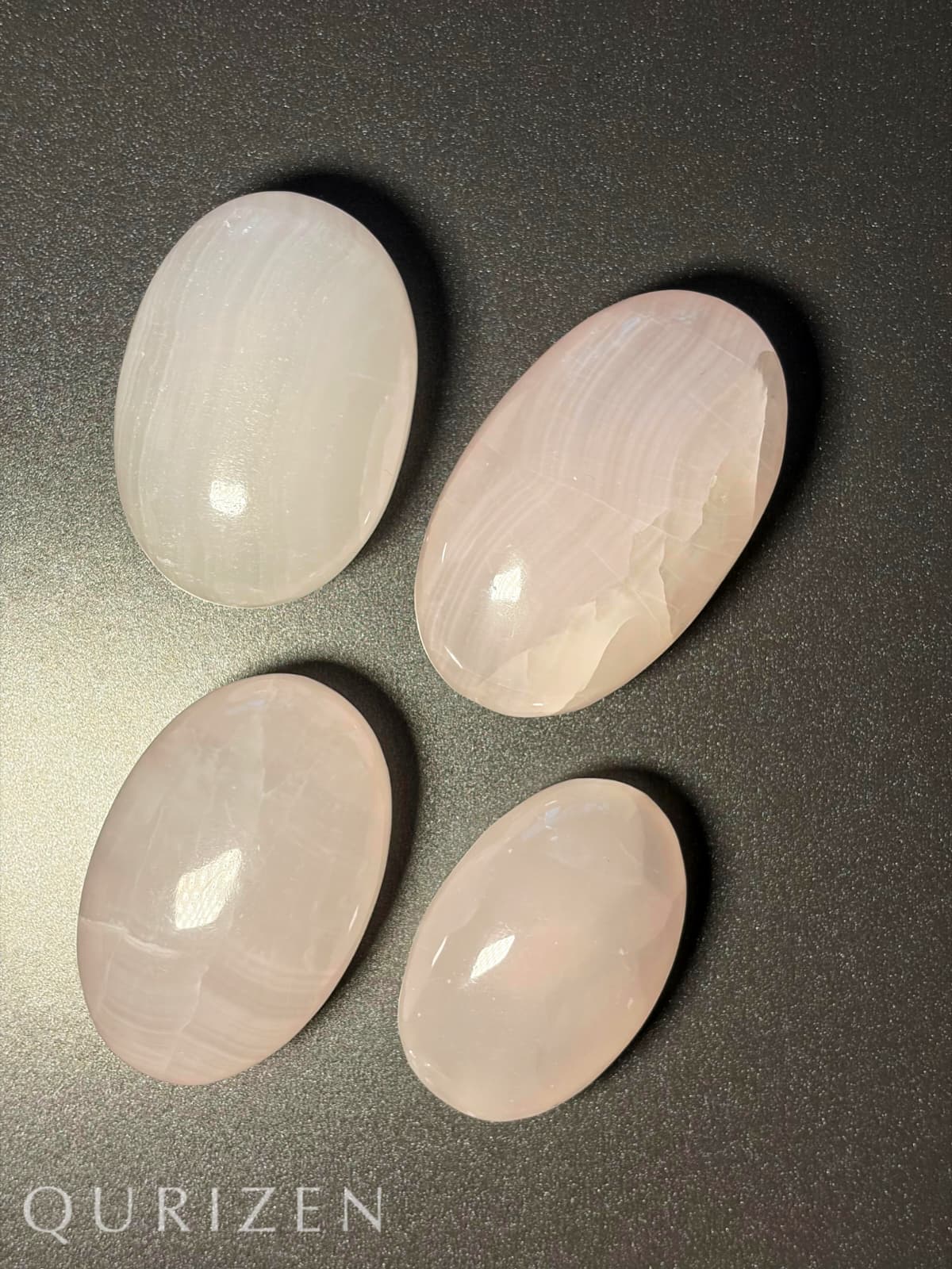 Four rose quartz stones on a dark surface with 'Qurizen' branding.