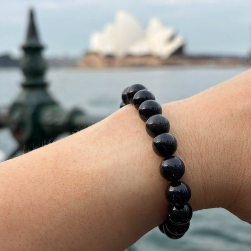 Black Obsidian beaded bracelet on a wrist with a blurred background of a famous landmark.
