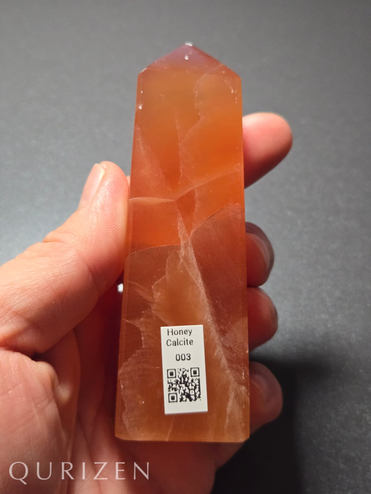 Orange crystal held in a hand with a QR code label, against a gray background