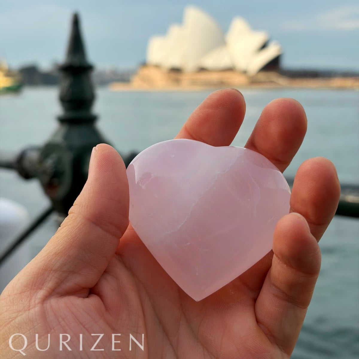 Heart-shaped pink stone held in a hand with a blurred background of a famous landmark.