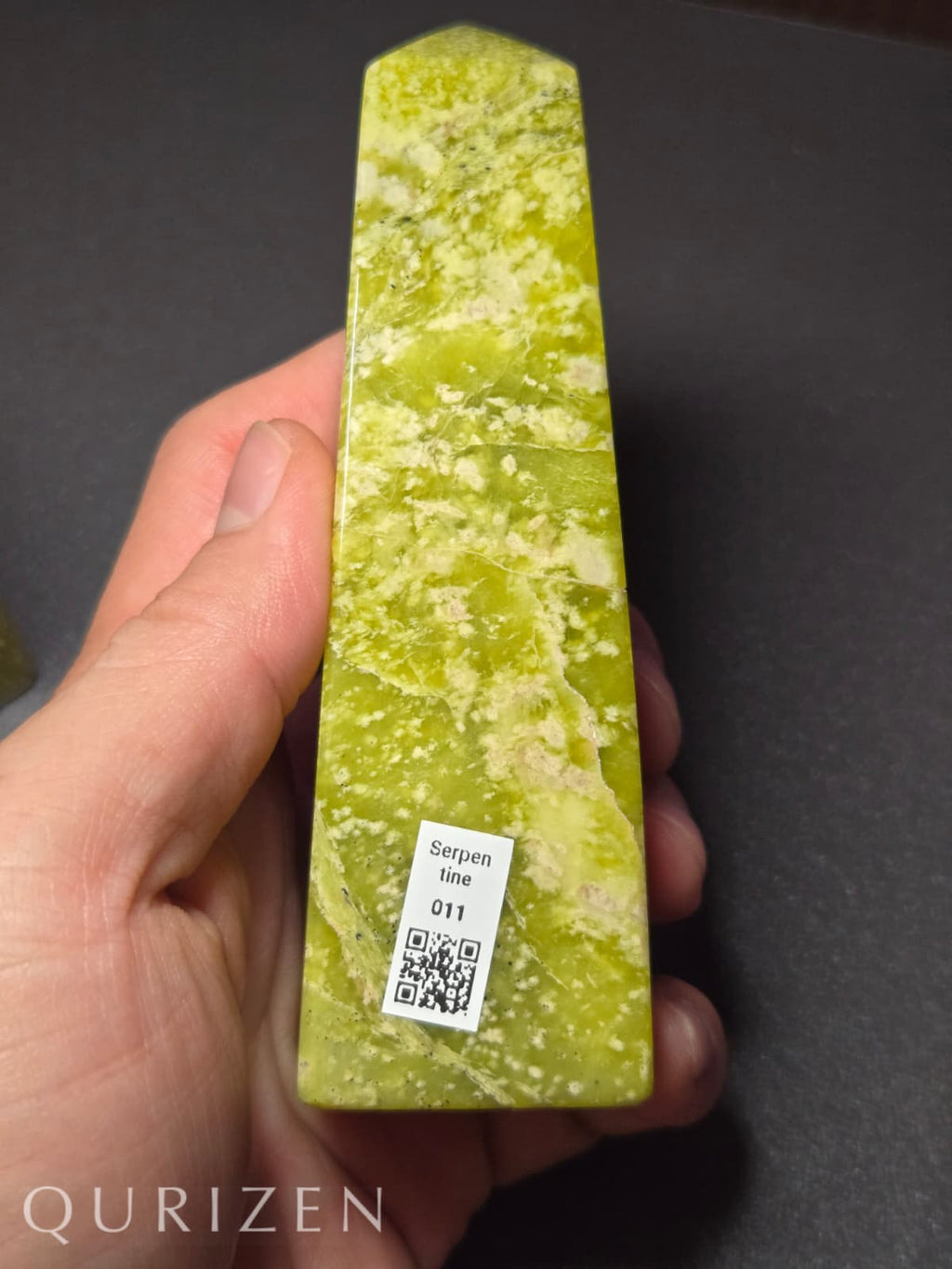 Green stone with a QR code label held by a hand on a dark background