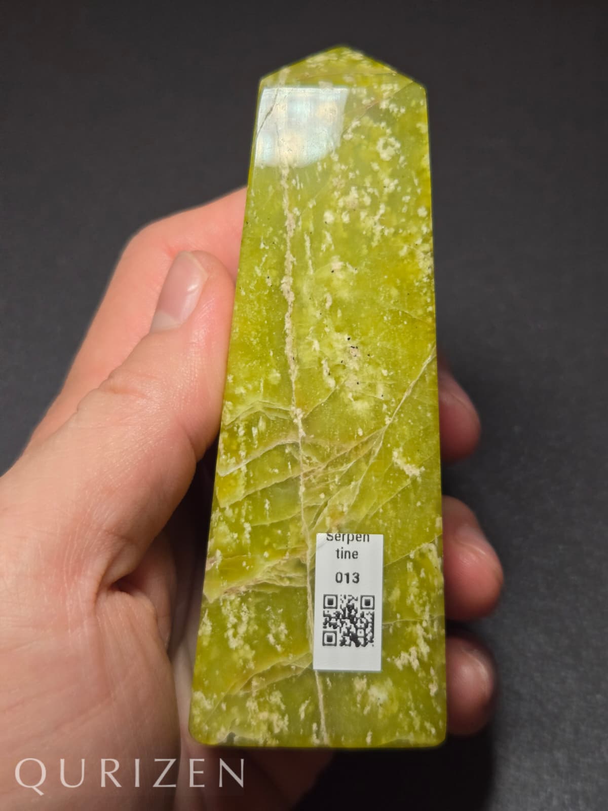 Green crystal held in a hand with a dark background, featuring the brand 'Qurizen'.