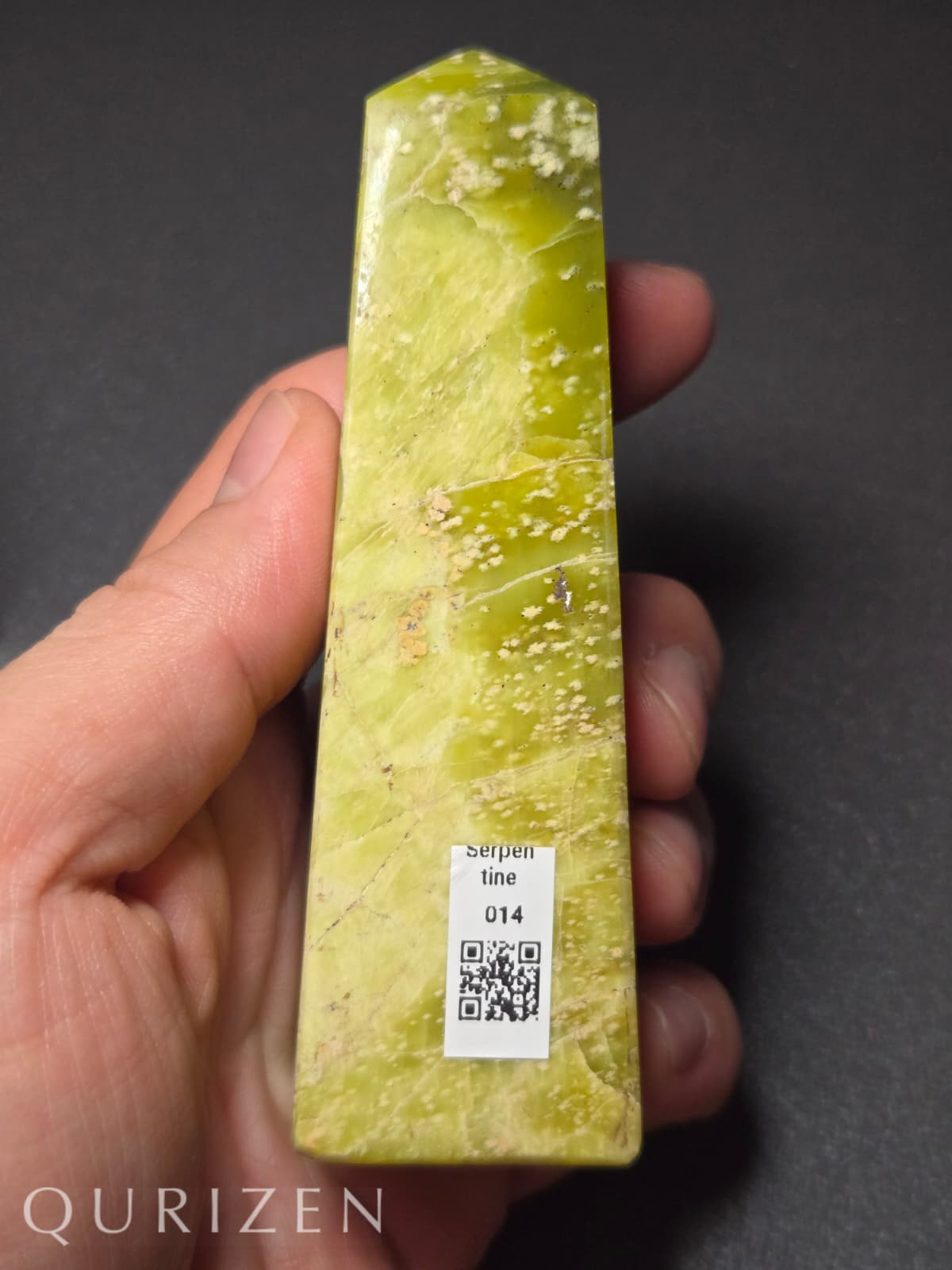 Green crystal held in a hand with a QR code label, against a dark background
